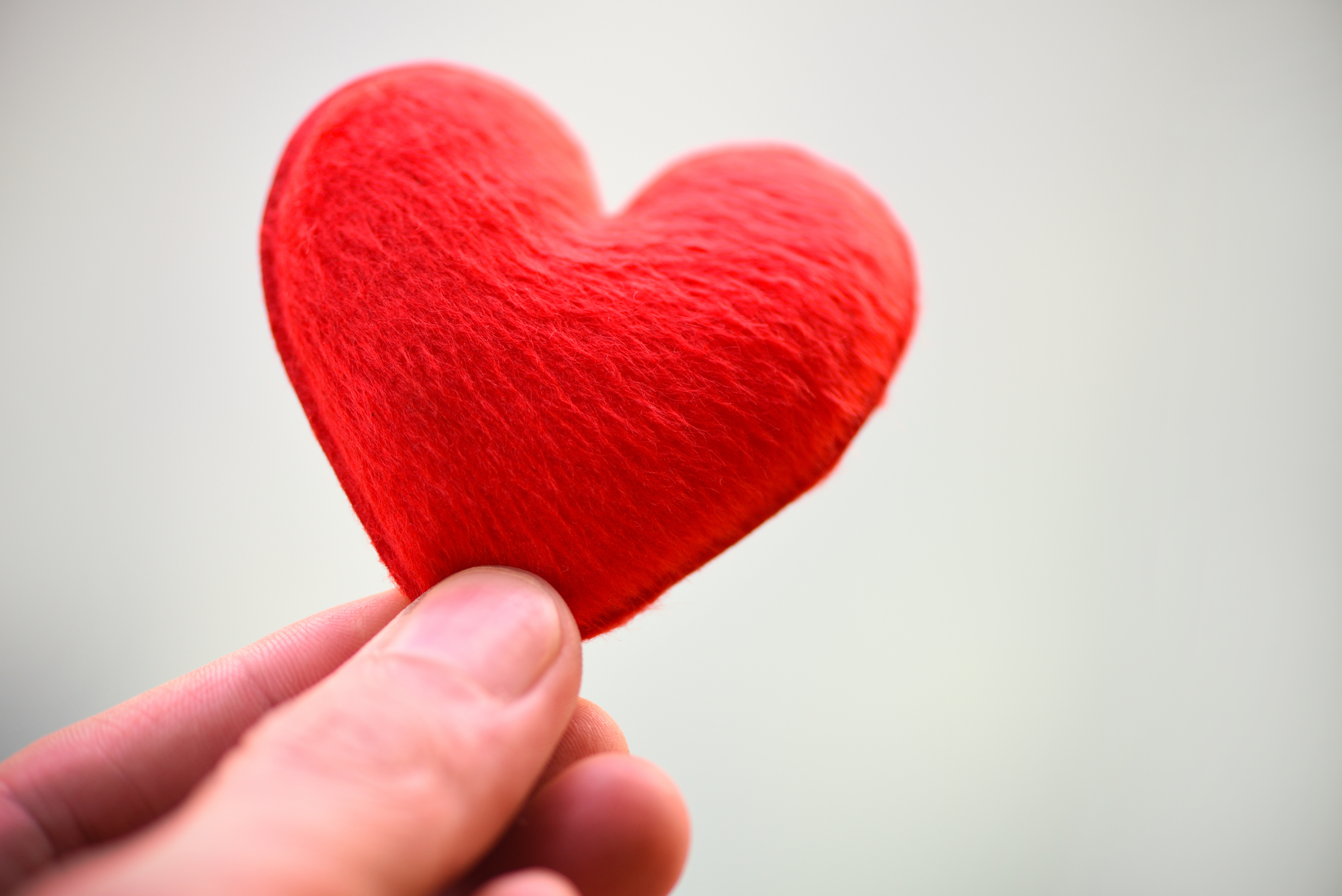 red heart held between a person's thumb and forefinger.